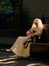 A woman in a headscarf, sitting on a bench in a shaft of sunlight, checks her phone. Shymkent, southern Kazakhstan