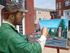 A lifelike artist statue paints a colorful outdoor scene on an easel.