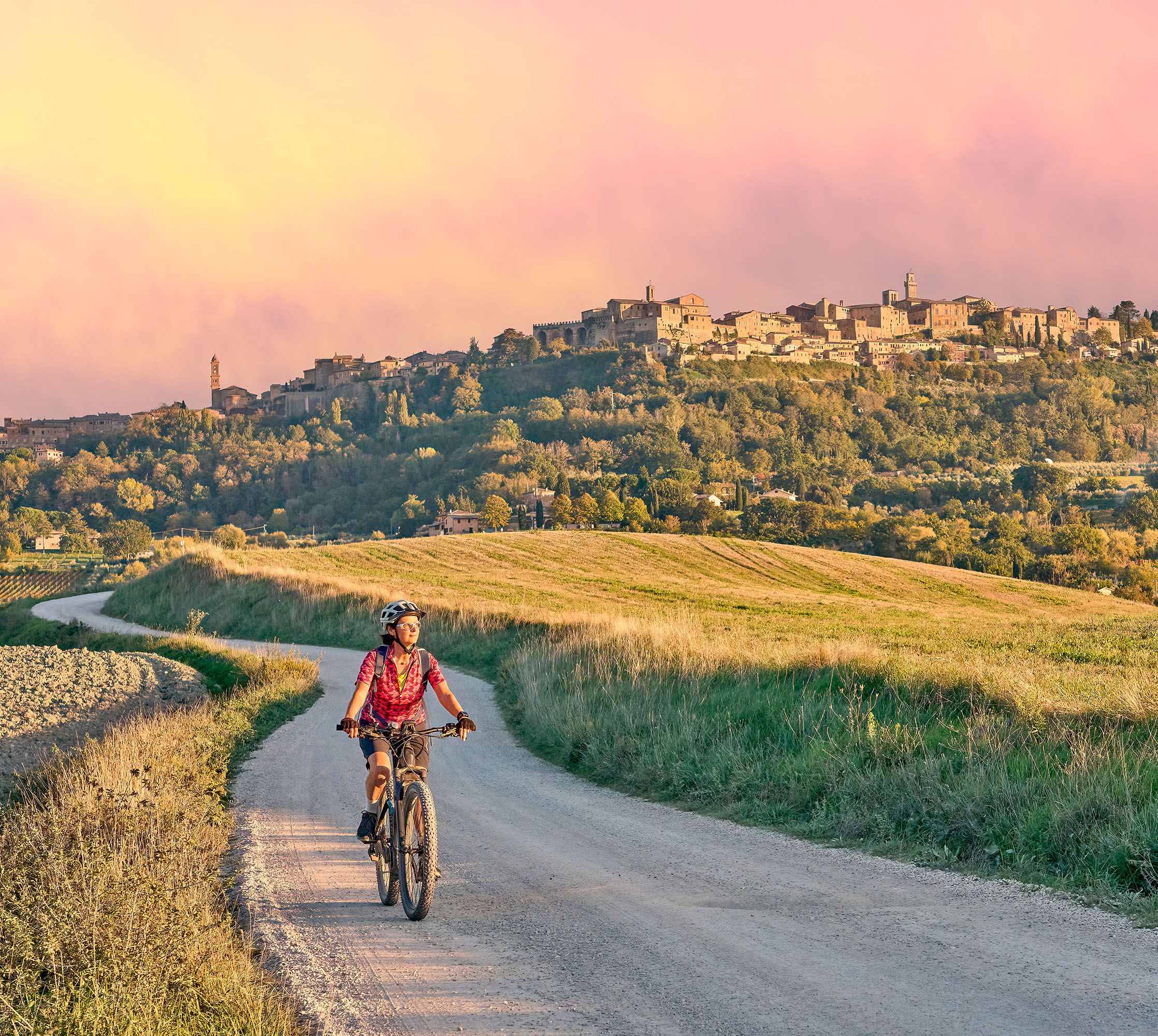 A woman rides her bicycle through the Italian countryside surrounded by rolling hills.