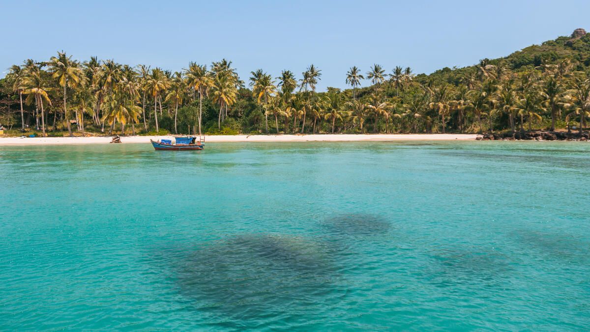 Beautiful coastal view of Phu Quoc Island sparkling under the sun with a traditional boat bobbing in the clear turquoise water.