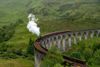 A steam train crossing the Glenfinnan Viaduct surrounded by lush green hills