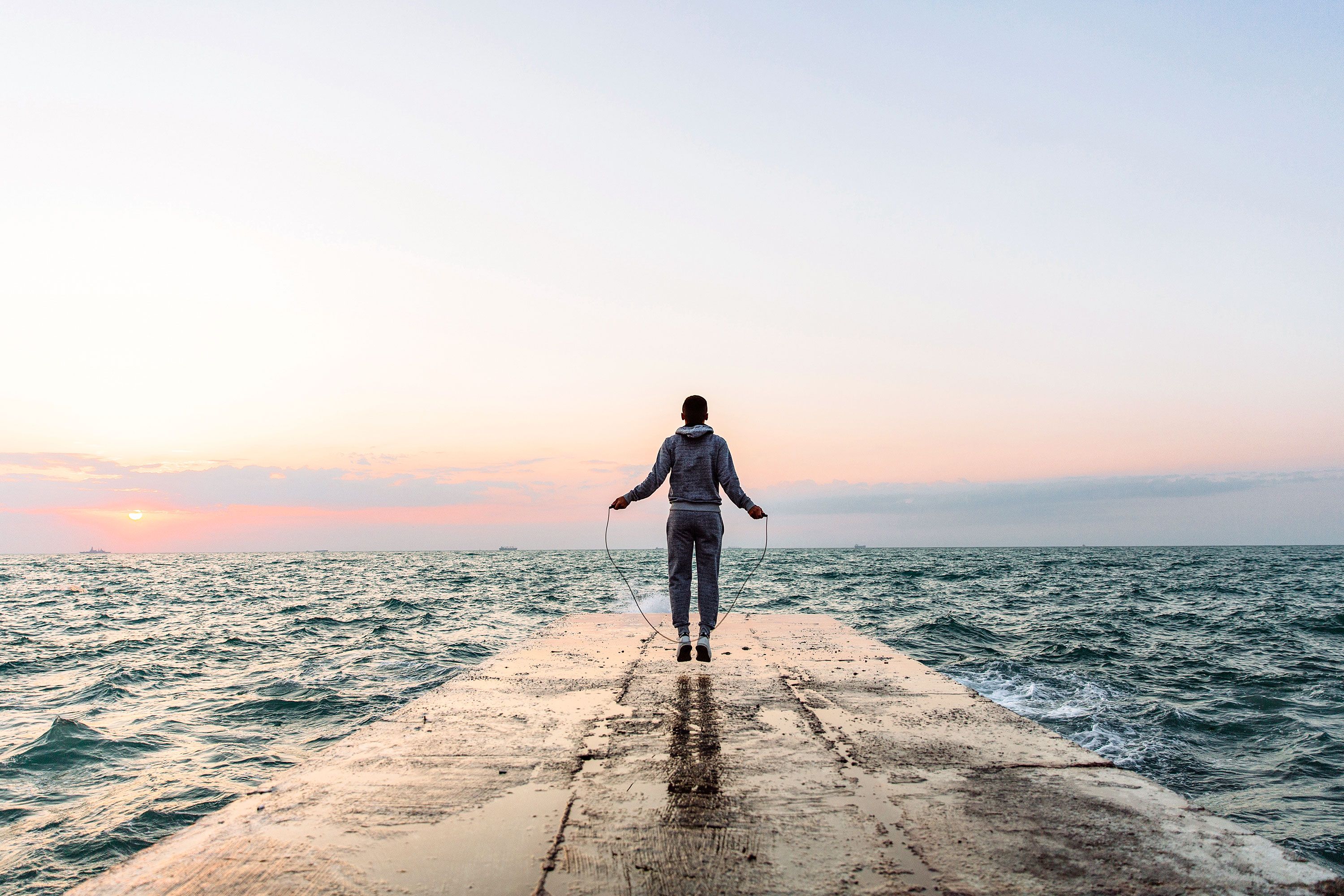 Man at the end of a concrete jetty jumps skips rope while surrounded by water.
