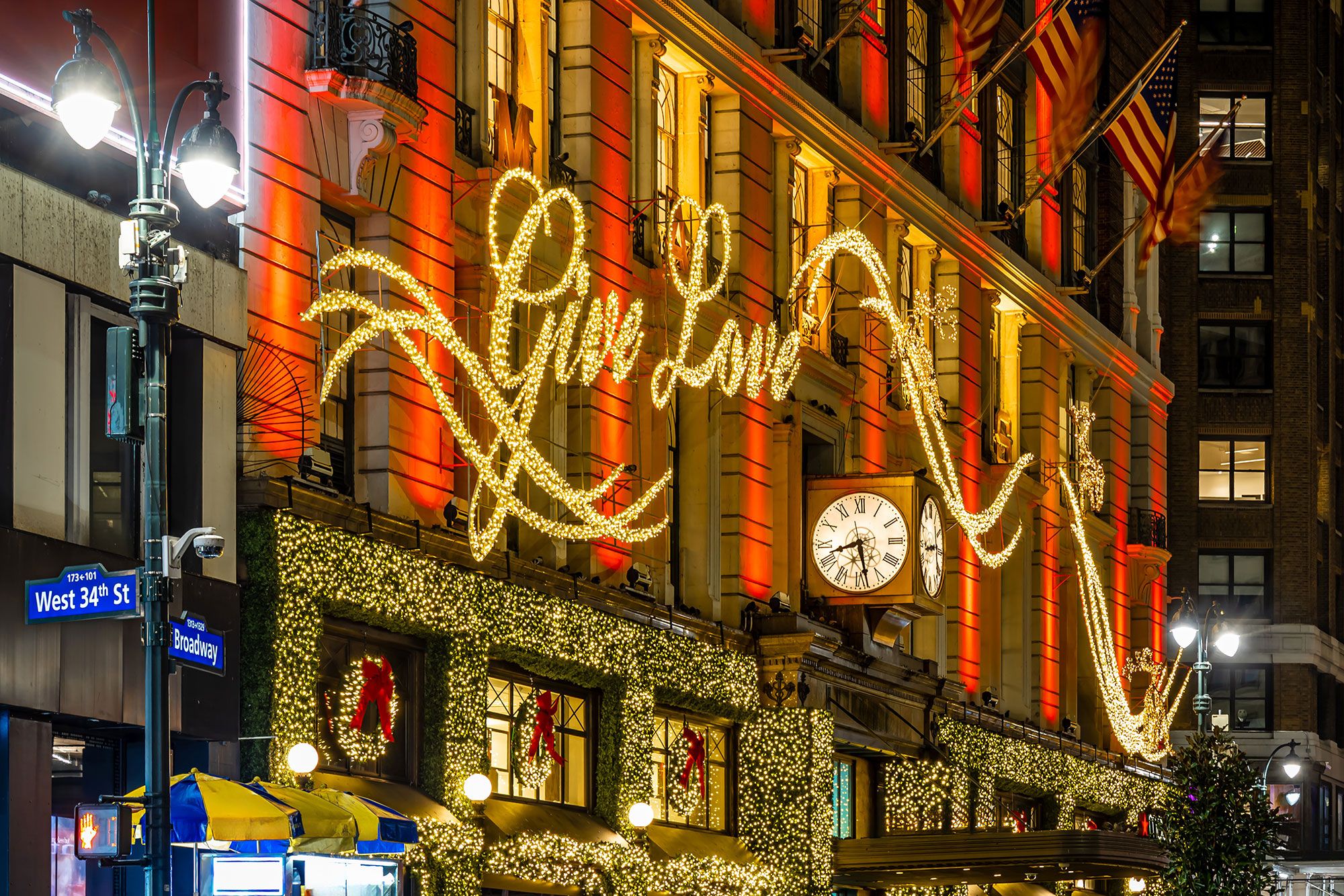 The facade of a building with large lights that read “Give Love” and Christmas wreaths underneath in an urban setting.