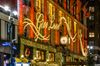 The facade of a building with large lights that read “Give Love” and Christmas wreaths underneath in an urban setting.