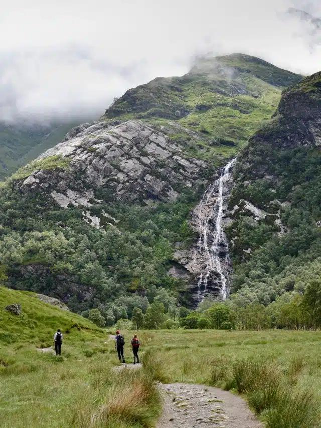 The cinematic Steall Falls in Glen Nevis run down a lush but rocky hillside with a trail in the foreground