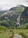 The cinematic Steall Falls in Glen Nevis run down a lush but rocky hillside with a trail in the foreground