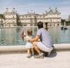 Seen from behind, a man crouches down next to a child at the edge of the Grand Bassin pool in the Jardin du Luxembourg, Paris, France