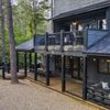 A black painted, wood paneled home in the woods, with a veranda on the upper floor
