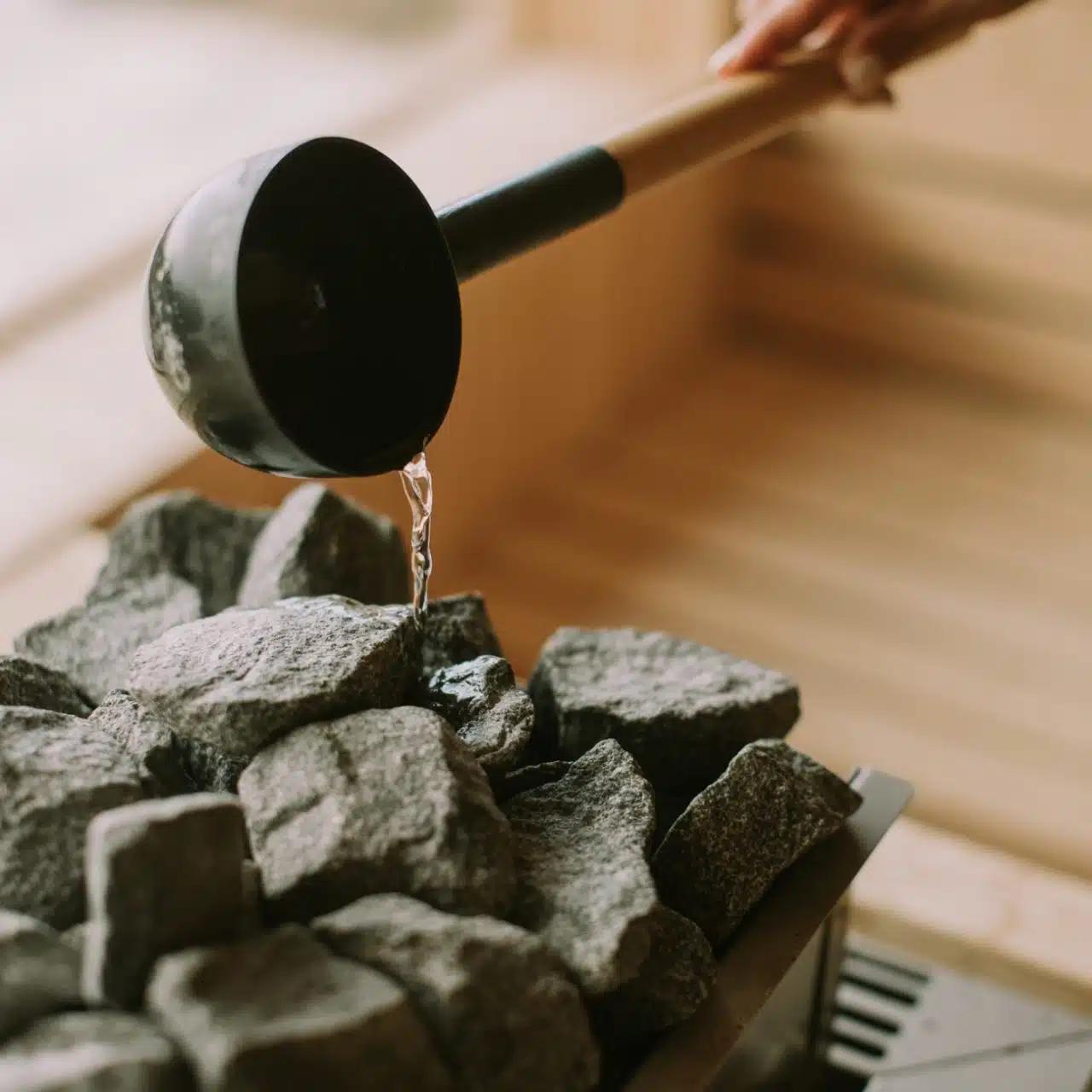 A hand ladles water over hot coals in a Swedish-style sauna