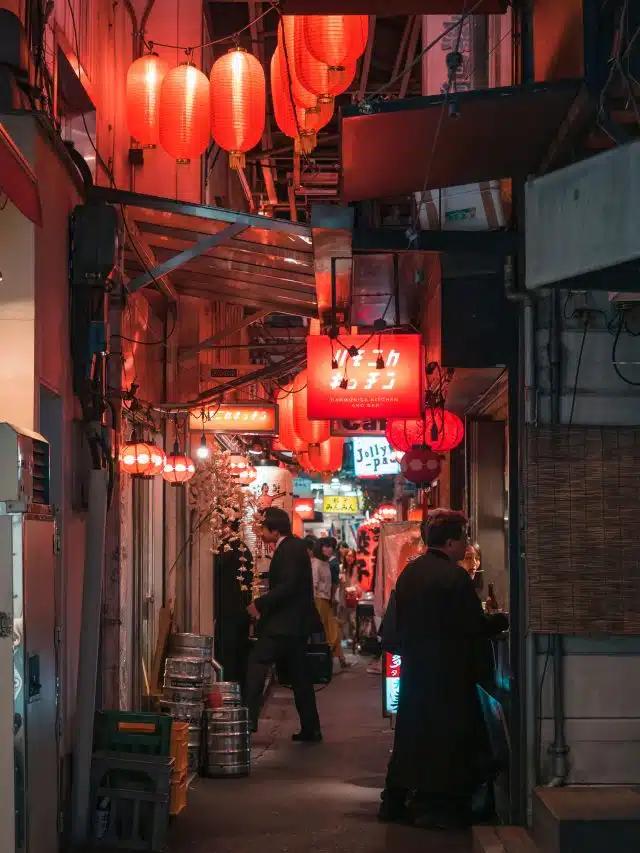 A narrow Tokyo street lined with restaurants, with red paper lanterns strung above