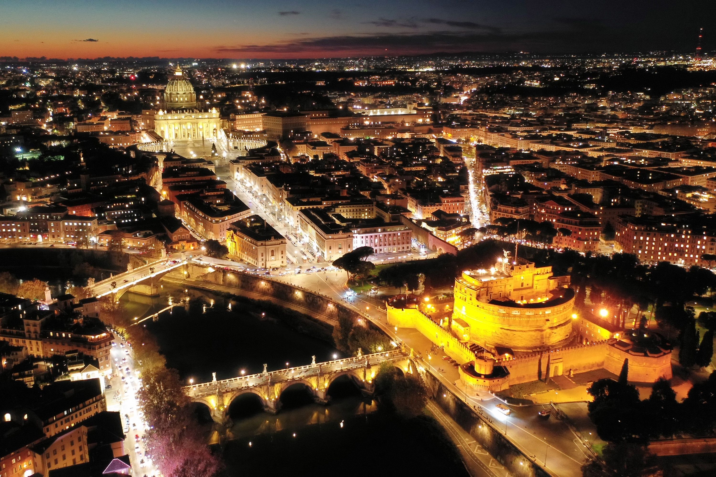 Aerial night view of an illuminated Castel Sant'Angelo and Saint Peter Basilica in Rome, Italy.