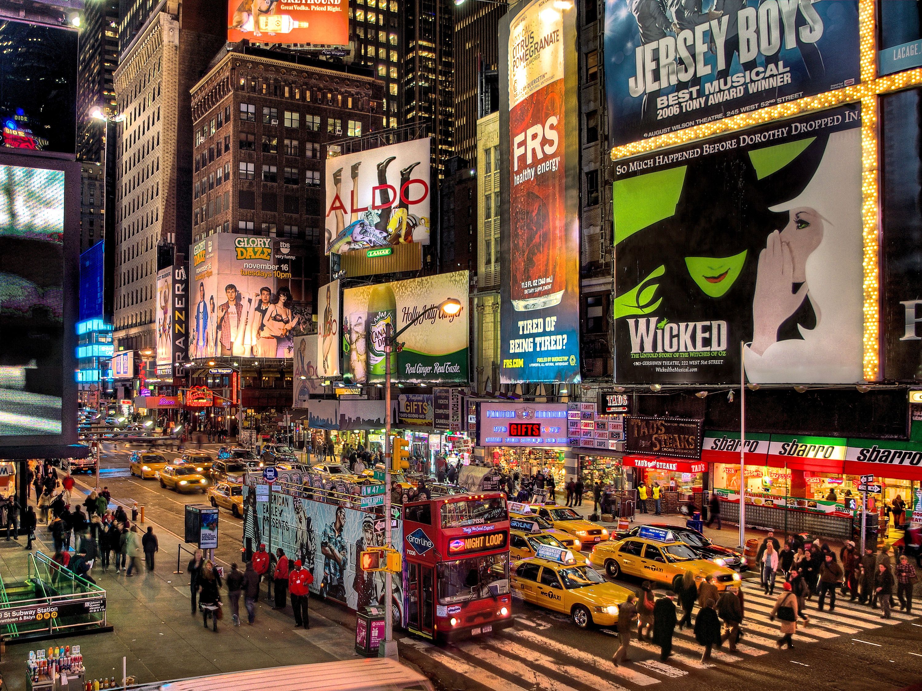 Busy street with theater signs, yellow taxi cabs and buses.