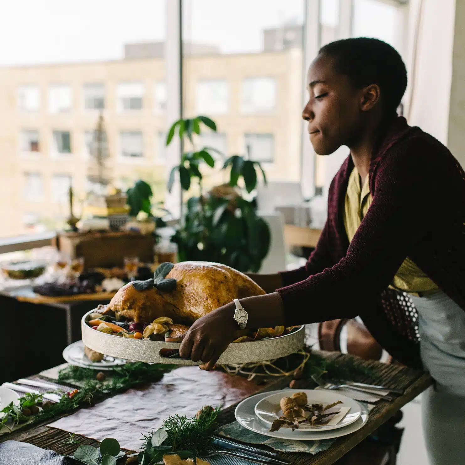 A woman brings a turkey to a table decorated with leaves and pine cones