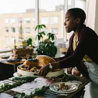 A woman brings a turkey to a table decorated with leaves and pine cones