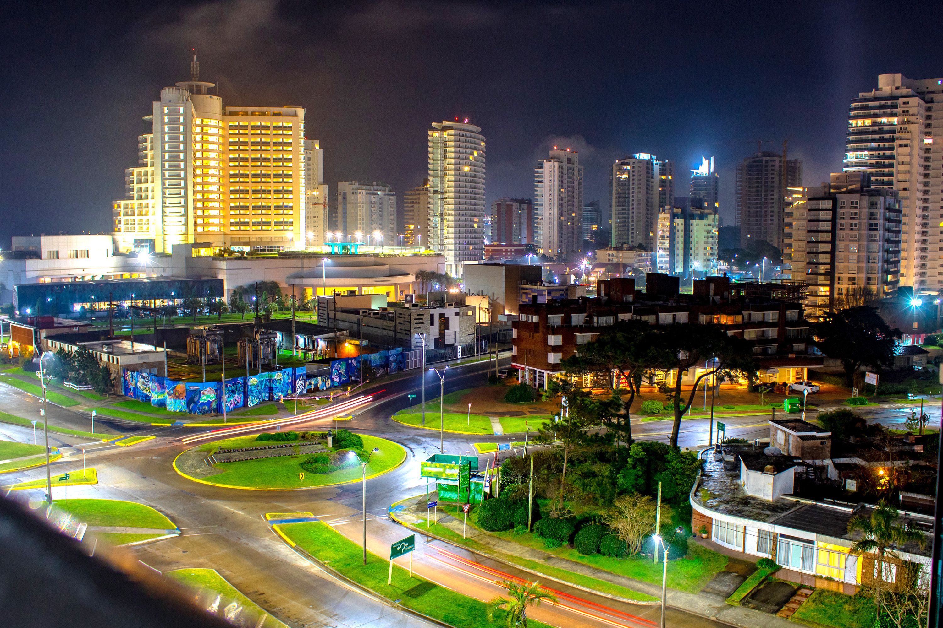 Night view of a city with palm trees and high-rise buildings.