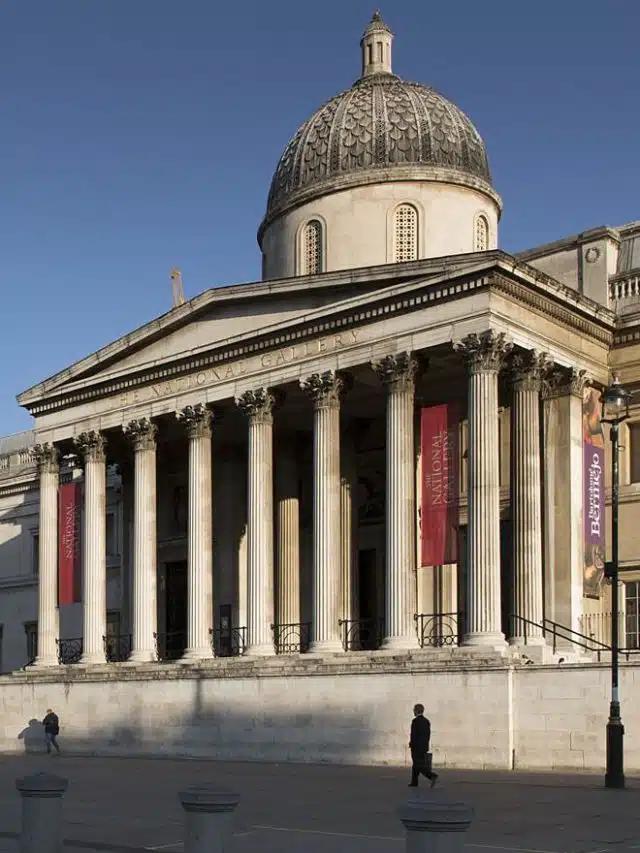 On a clear day with blue skies, sun shines on the columnated facade of the National Gallery in London, England