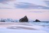 Large, craggy rocks rise out of the sand on Currumbin Alley beach with the Gold Coast skyline in the background