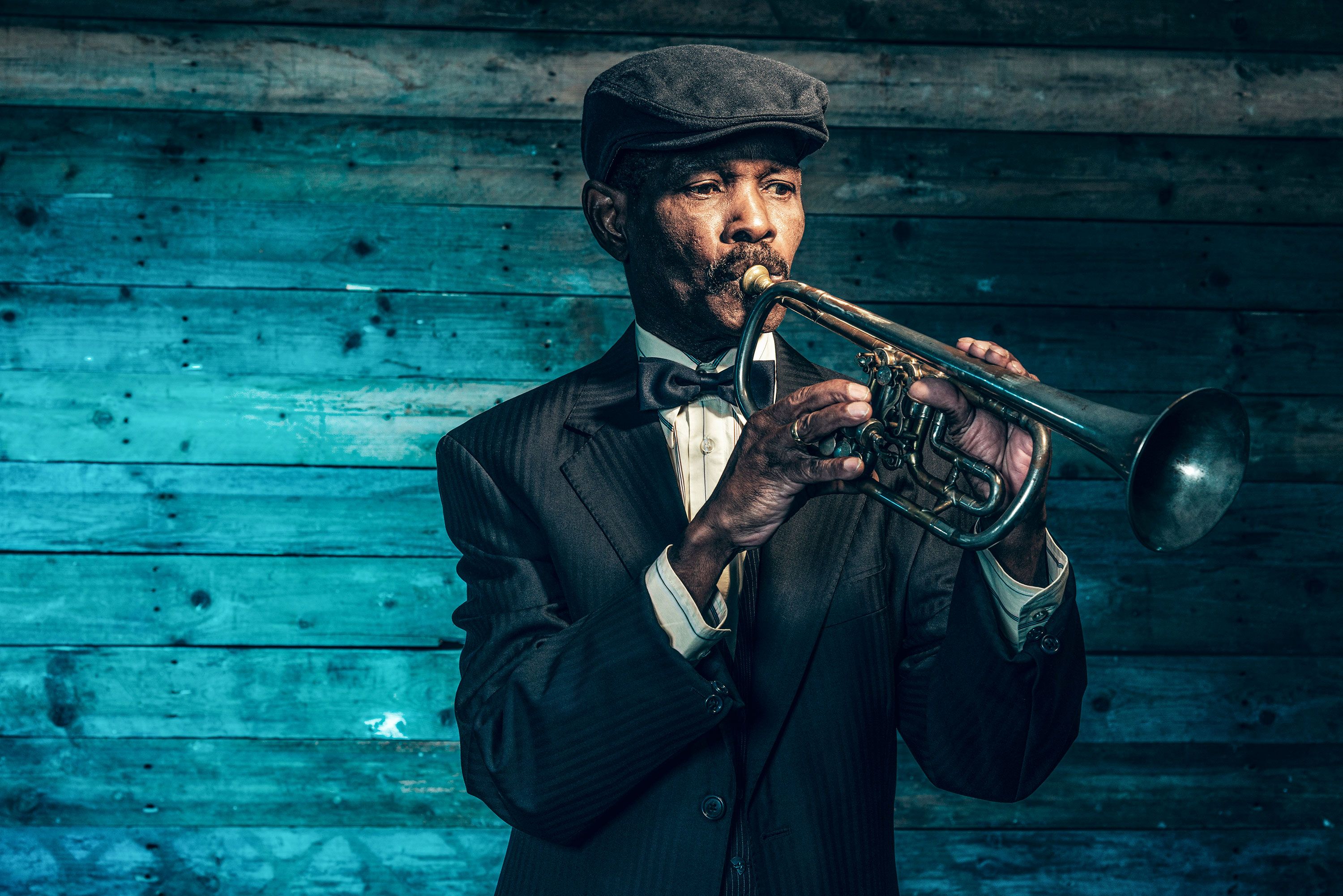 Senior African American jazz musician in vintage clothing plays trumpet.
