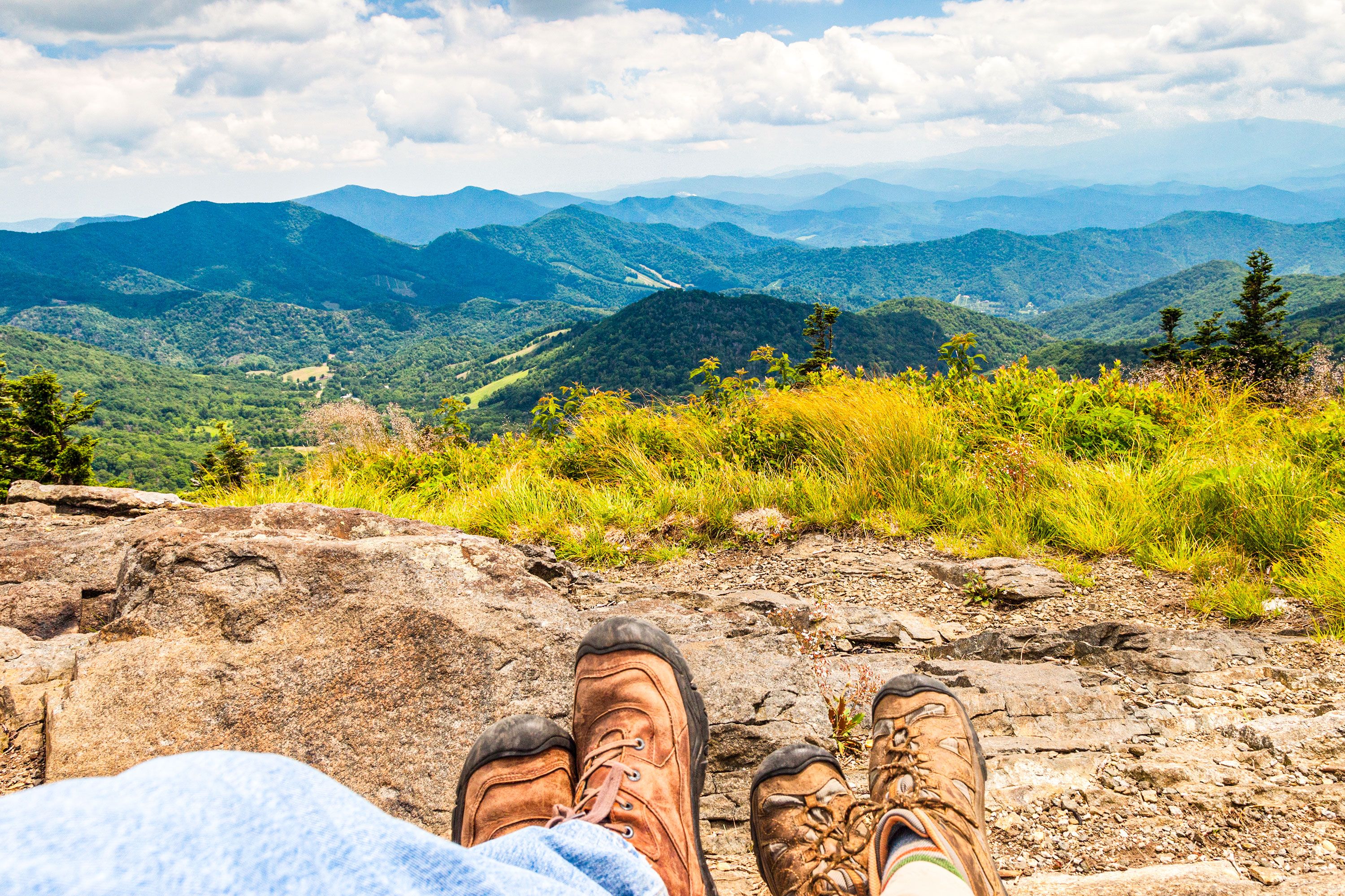 Perspective with boots in the foreground looking out over green mountains.