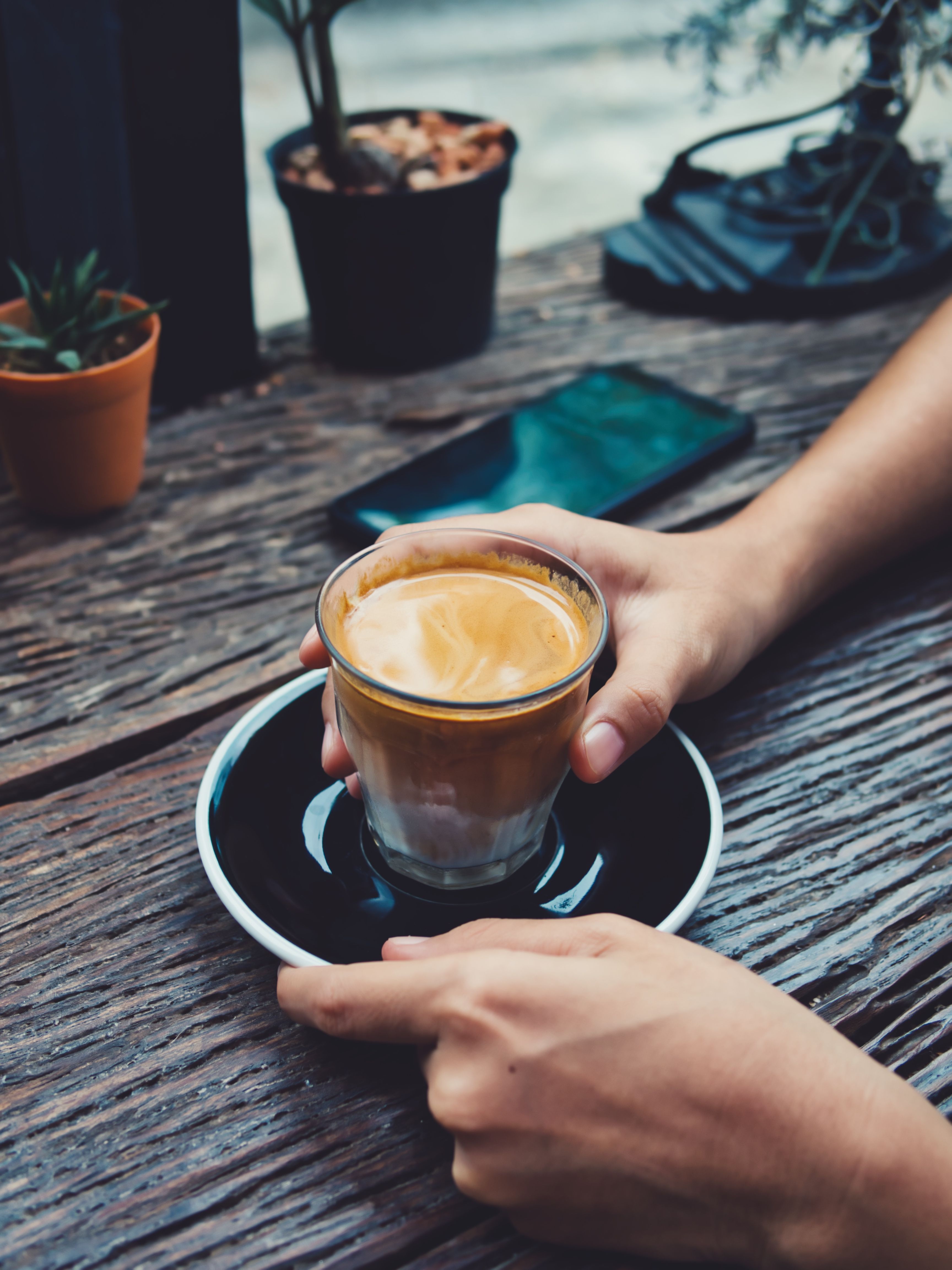 Two hands holding a coffee in a glass on a black saucer 