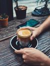 Two hands holding a coffee in a glass on a black saucer