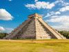 A large stone pyramid with steps on either side on a sunny day with clouds in the sky.