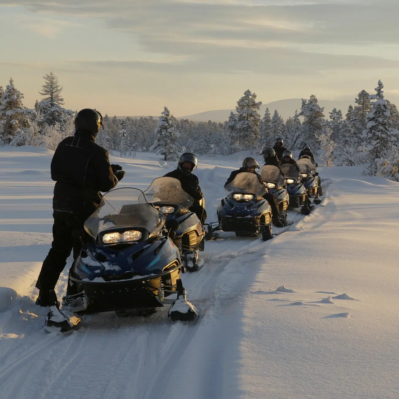 Snowmobiles and their riders, wrapped up warm and wearing motorcycle helmets, ready for a ride into the snowy forest in Yellowknife
