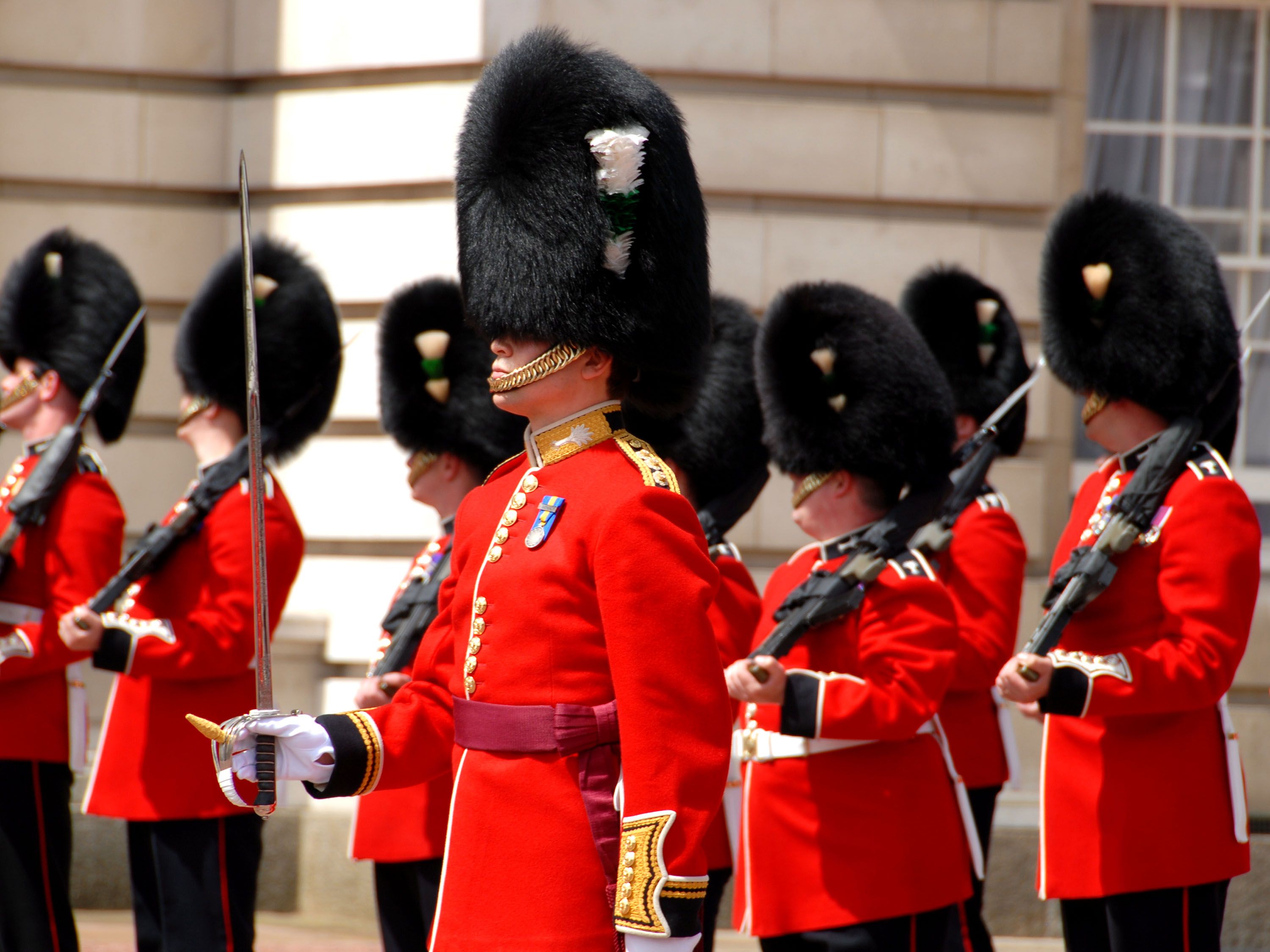 British guards with red uniforms and black hats outside Buckingham Palace.