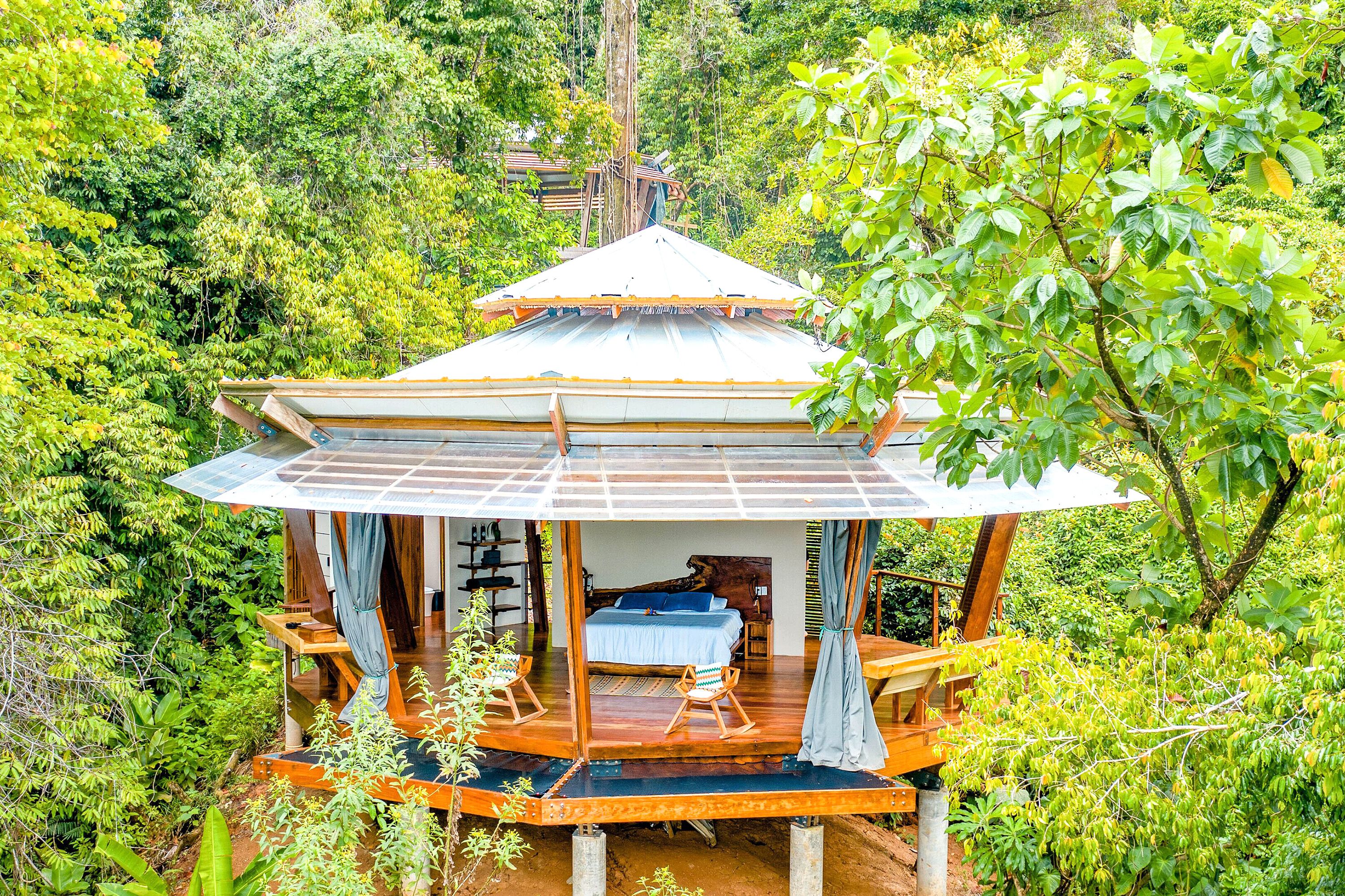An open air treehouse hotel room with a bed, chairs and curtains.