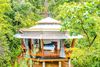 An open air treehouse hotel room with a bed, chairs and curtains.
