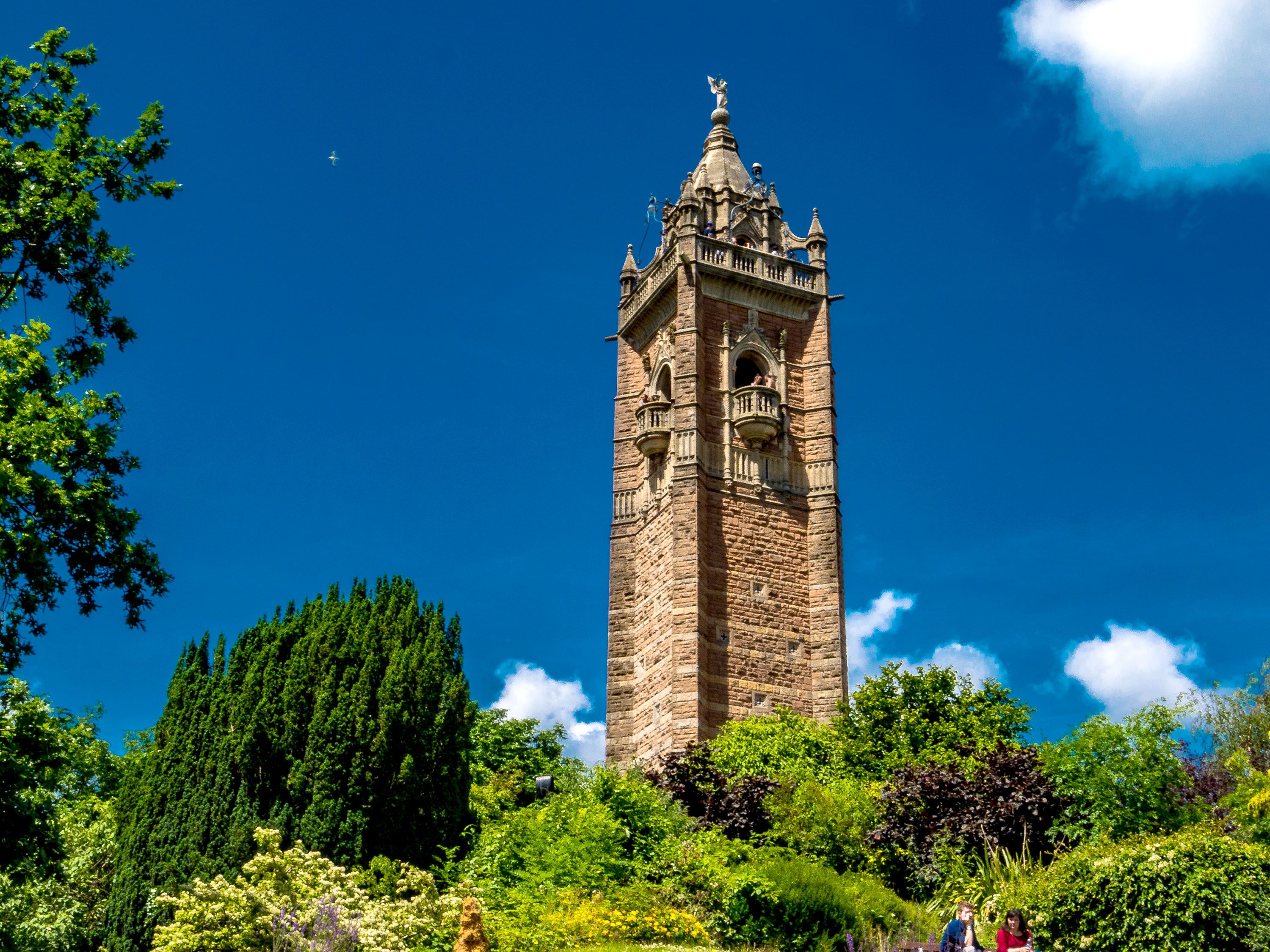 Large tower peeking over trees against a bright blue sky.