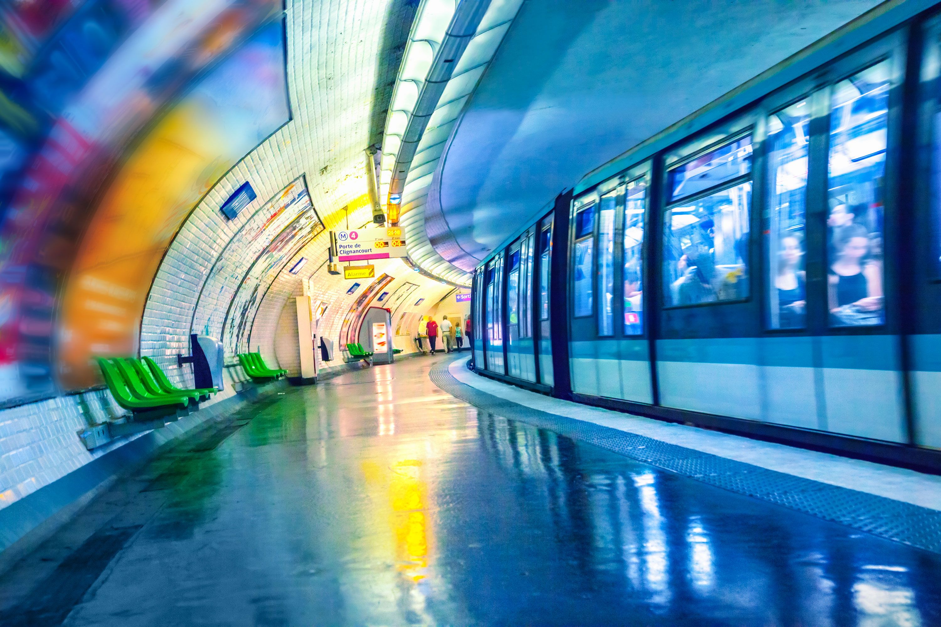 Interior view of a Paris Metro station with colorful light reflections as a subway train passes in motion blur