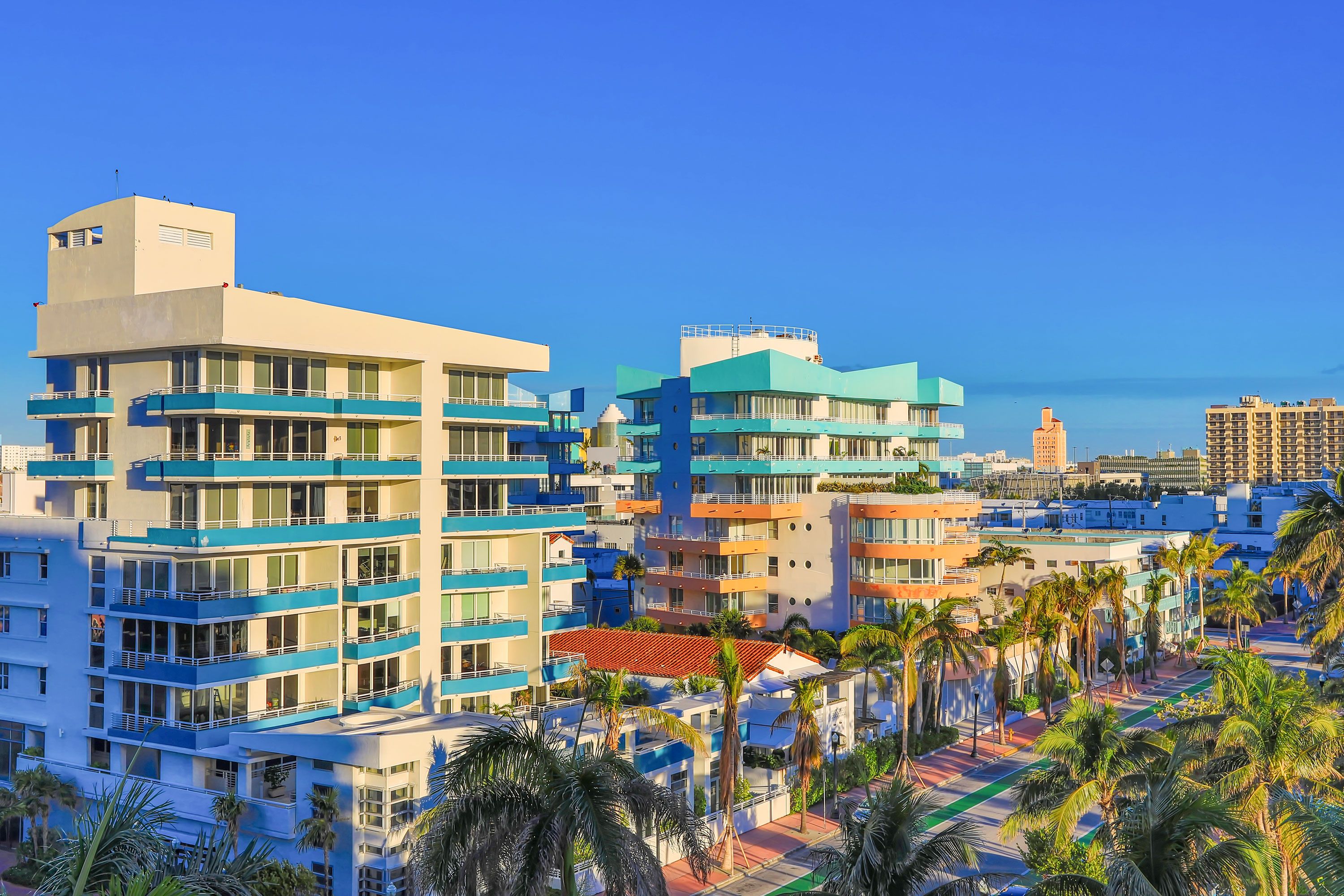Elevated view of art deco bulidngs with balconies with palm trees and bright blue sky.