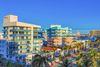 Elevated view of art deco bulidngs with balconies with palm trees and bright blue sky.