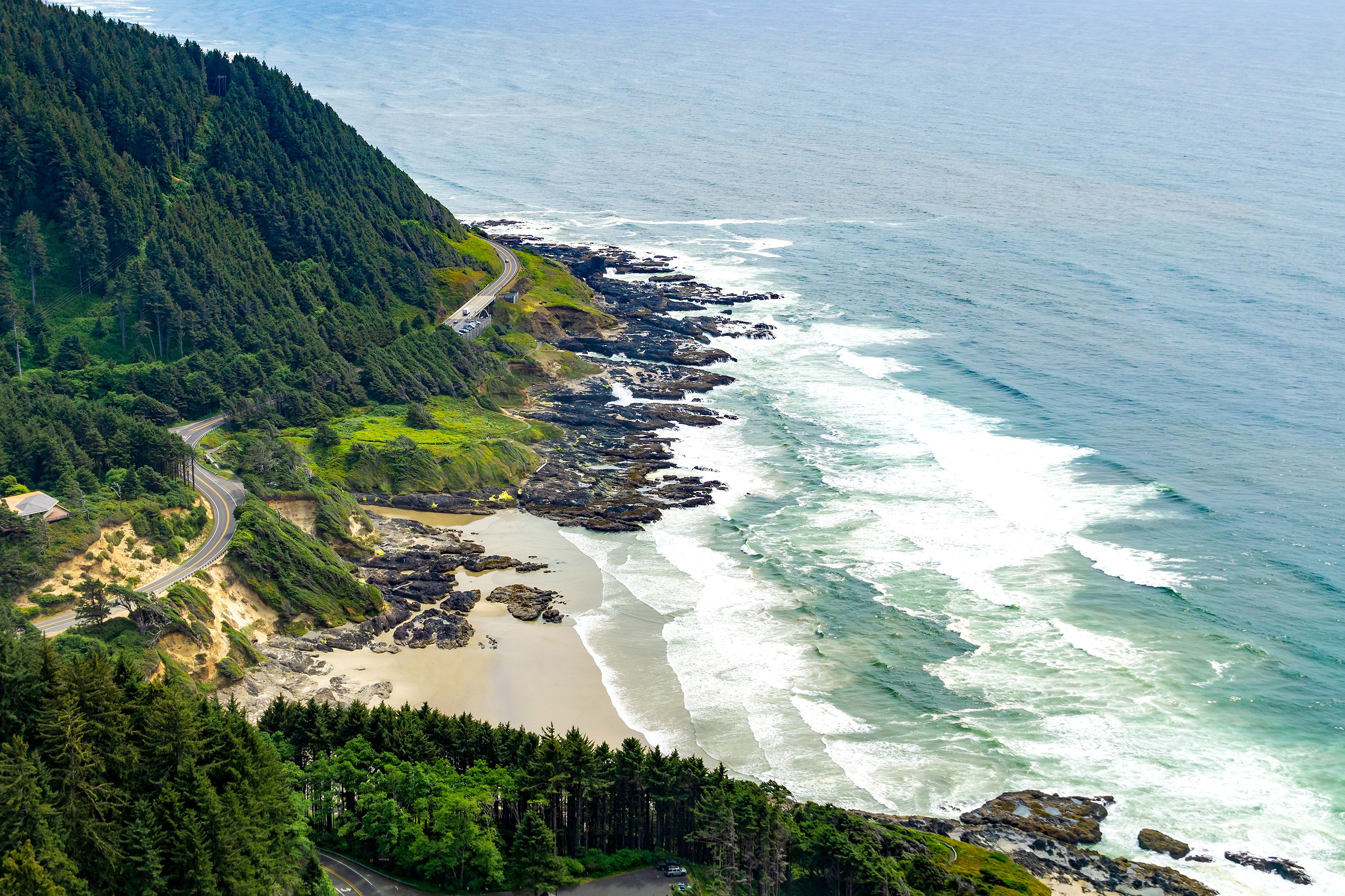 A sandy cove featuring rock formations, surrounded by green forest.