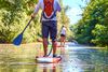 Close up of man's legs on stand up paddle board and woman paddleboarder in water in mangrove.