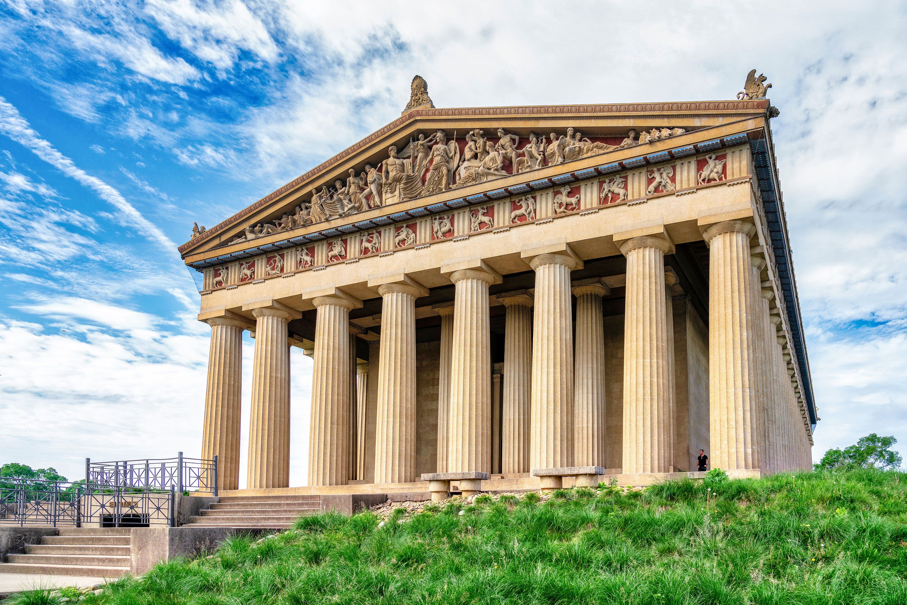 Classic Greek temple type building with columns, green grass and cloudy sky.