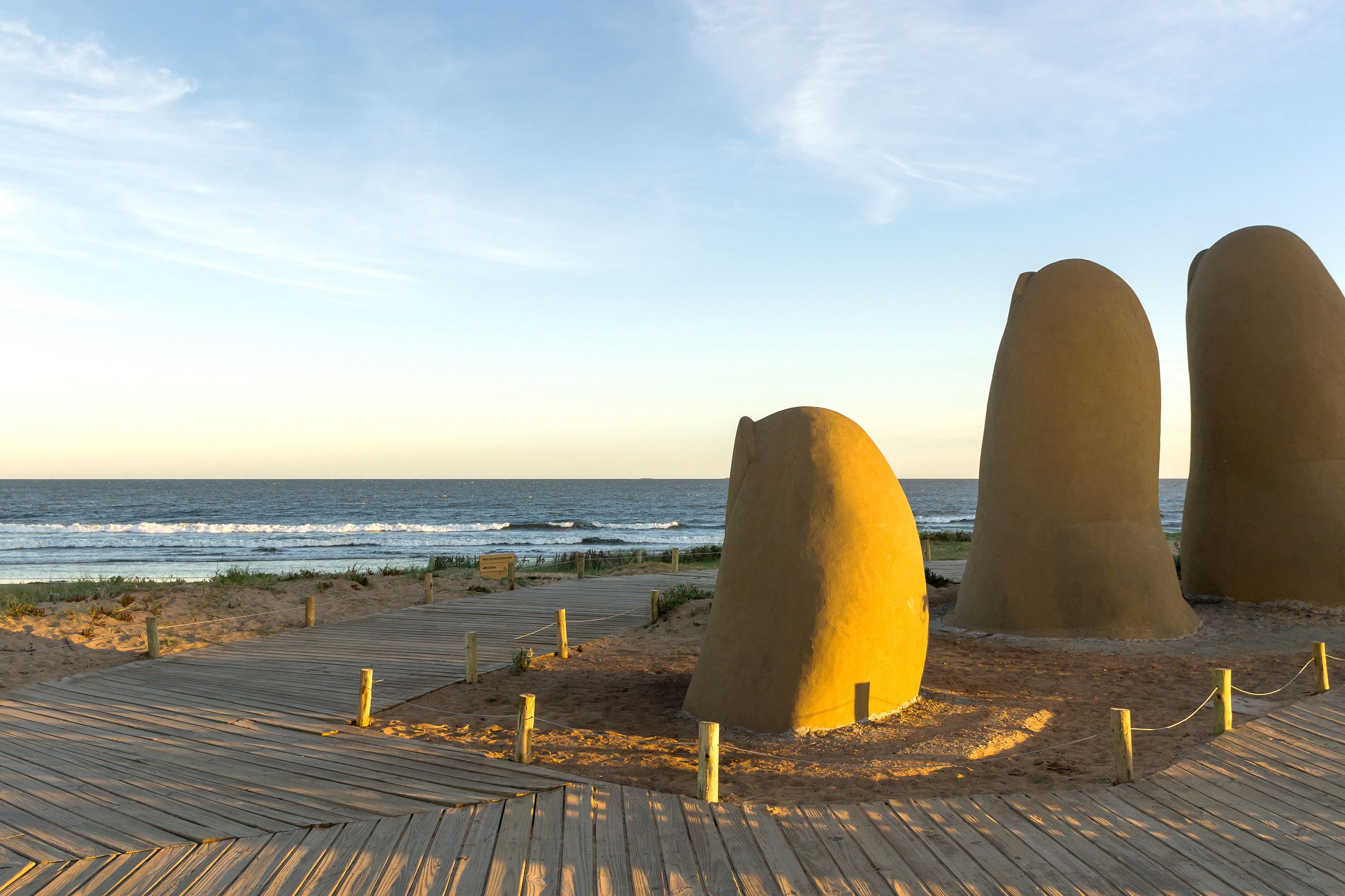 The sun rises on a beach area where a giant sculpture of fingers emerging from the sand is on display.