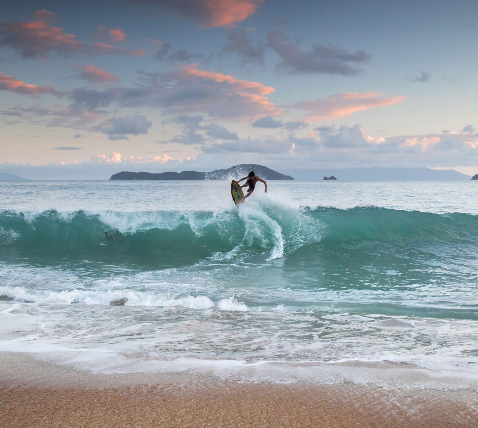 A surf boarder makes a jump on a turquoise wave at dusk, São Paulo