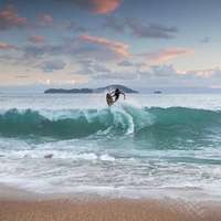 A surf boarder makes a jump on a turquoise wave at dusk, São Paulo