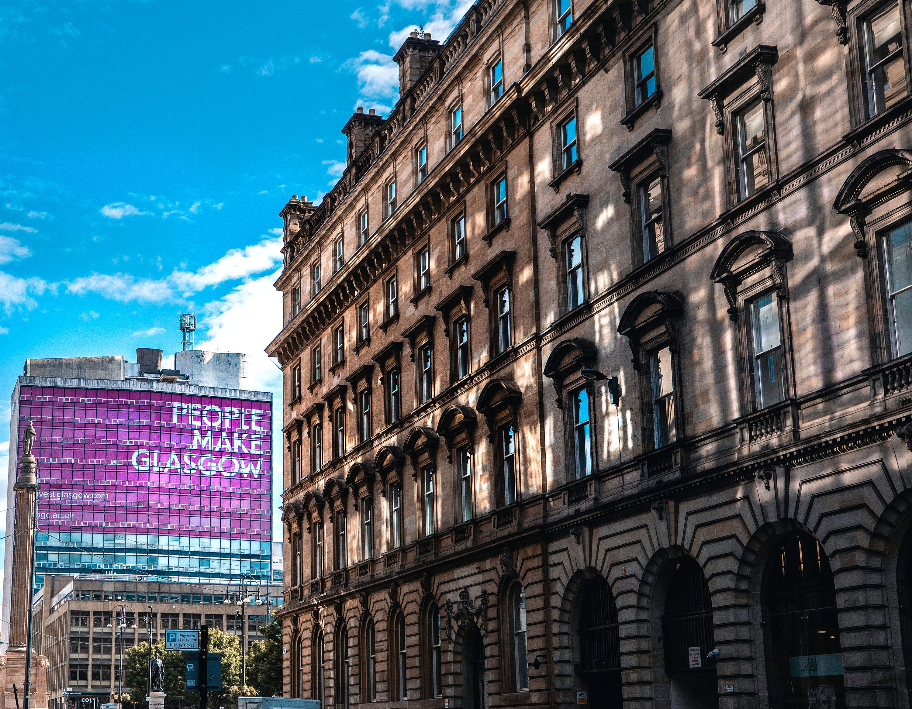 Five-story building with arched doorways and People Make Glasgow billboard.