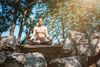 A woman meditating around a stack of large rocks with trees in the background.