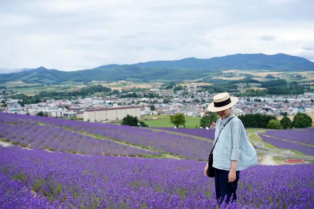 A woman wearing a straw boater hat walks among lavender fields in Hokkaido, Japan