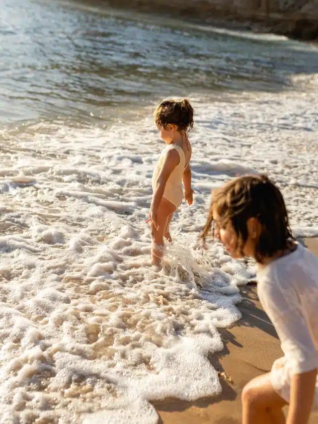 Two young children are playing in the low, foamy waves on the shores of a beach in Playa del Carmen, Mexico