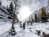 A person with a red coat walks on a snow-filled trail surrounded by trees.