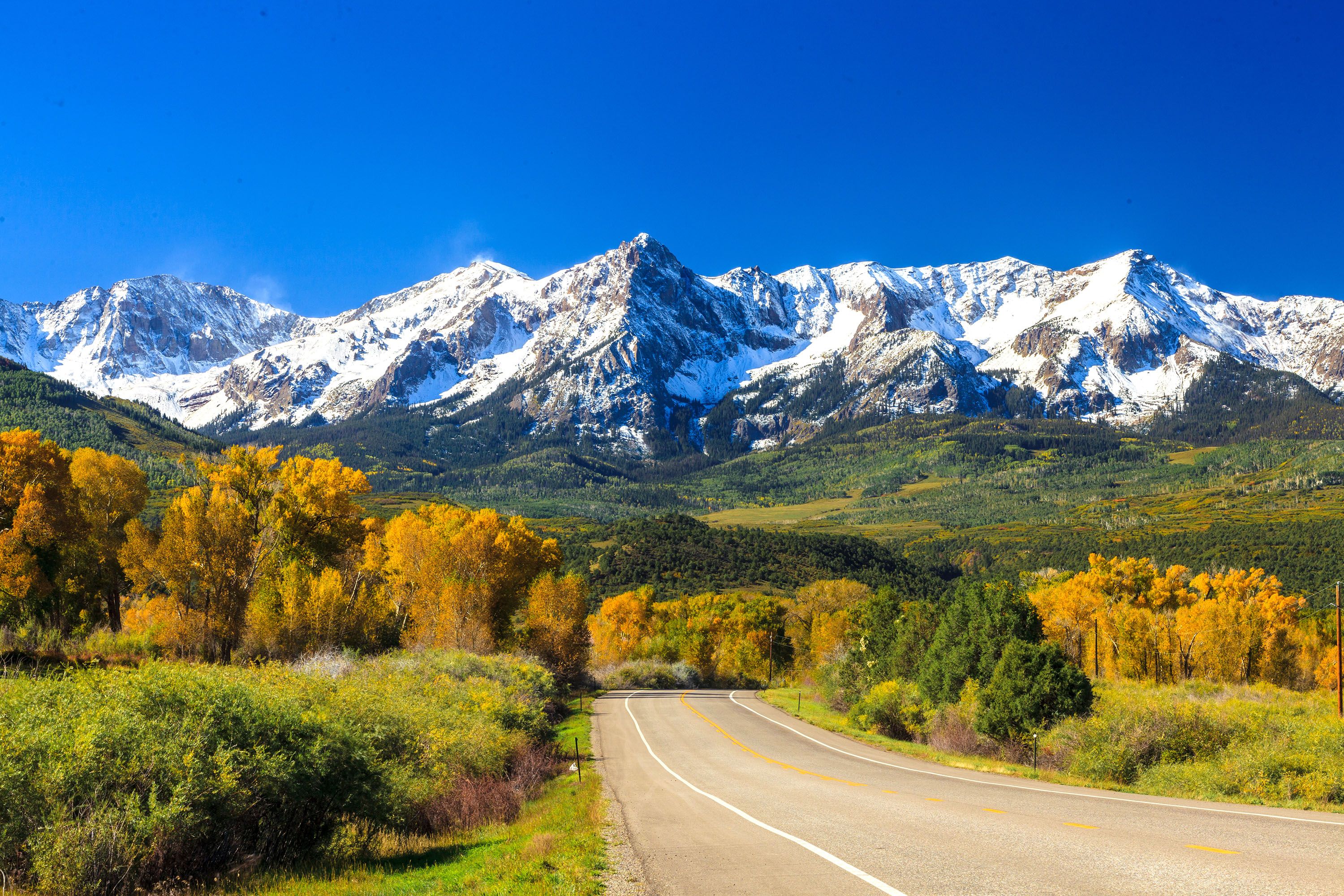 A road in lush green valley, snow-capped mountains in the background.