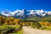 A road in lush green valley, snow-capped mountains in the background.