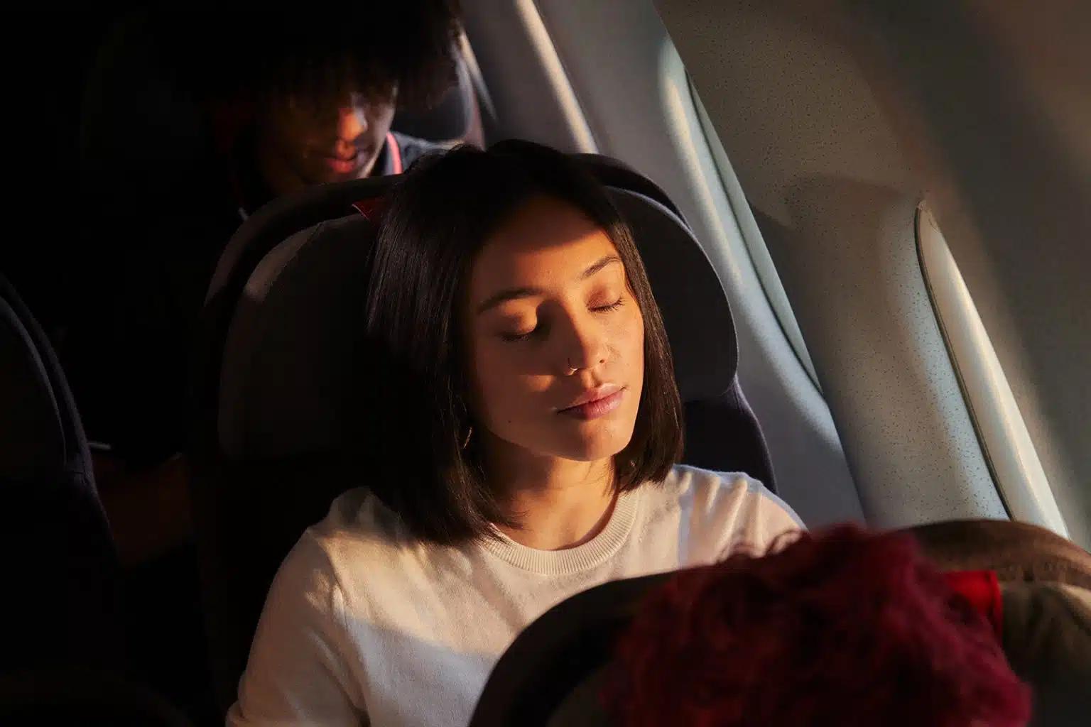 A woman sitting on an airplane closes her eyes peacefully
