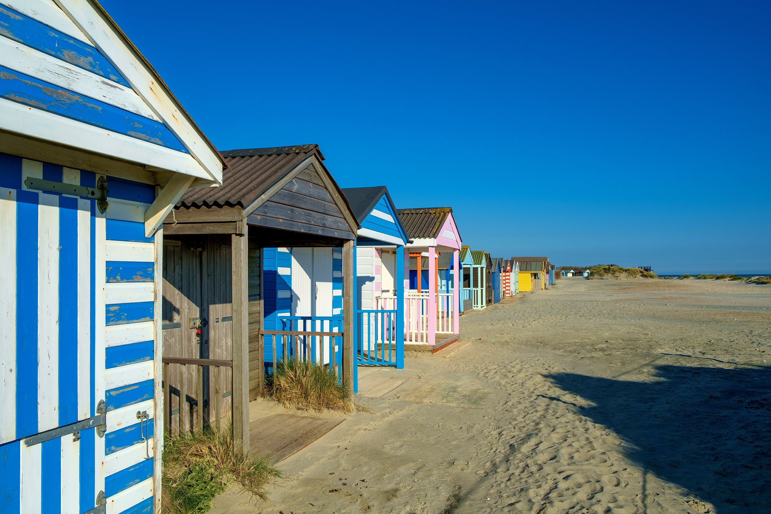 Blue and white striped and colorful beach shacks in a row on a beach.