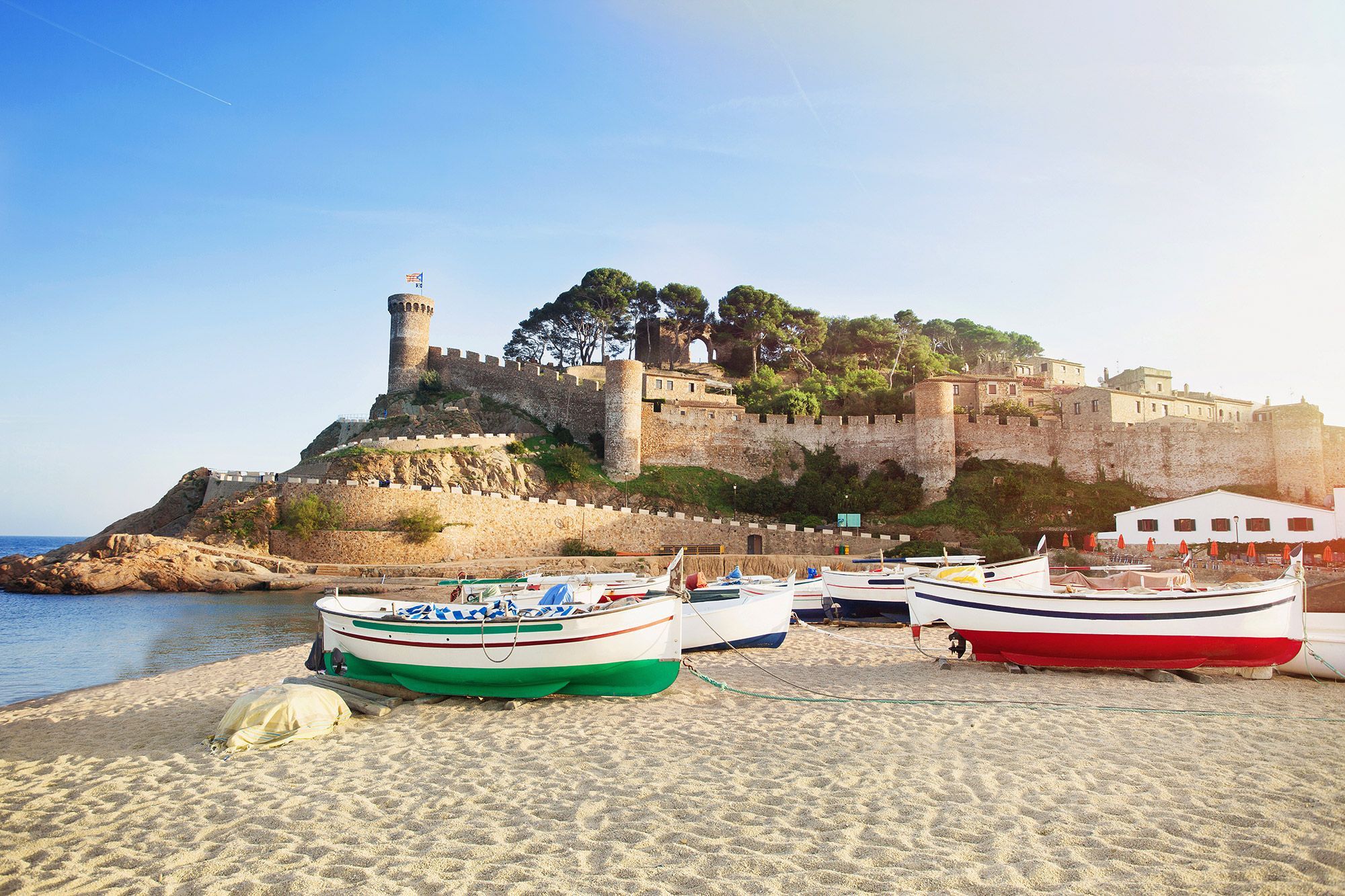 Boats on the beach with a brick wall and building behind in Spain.